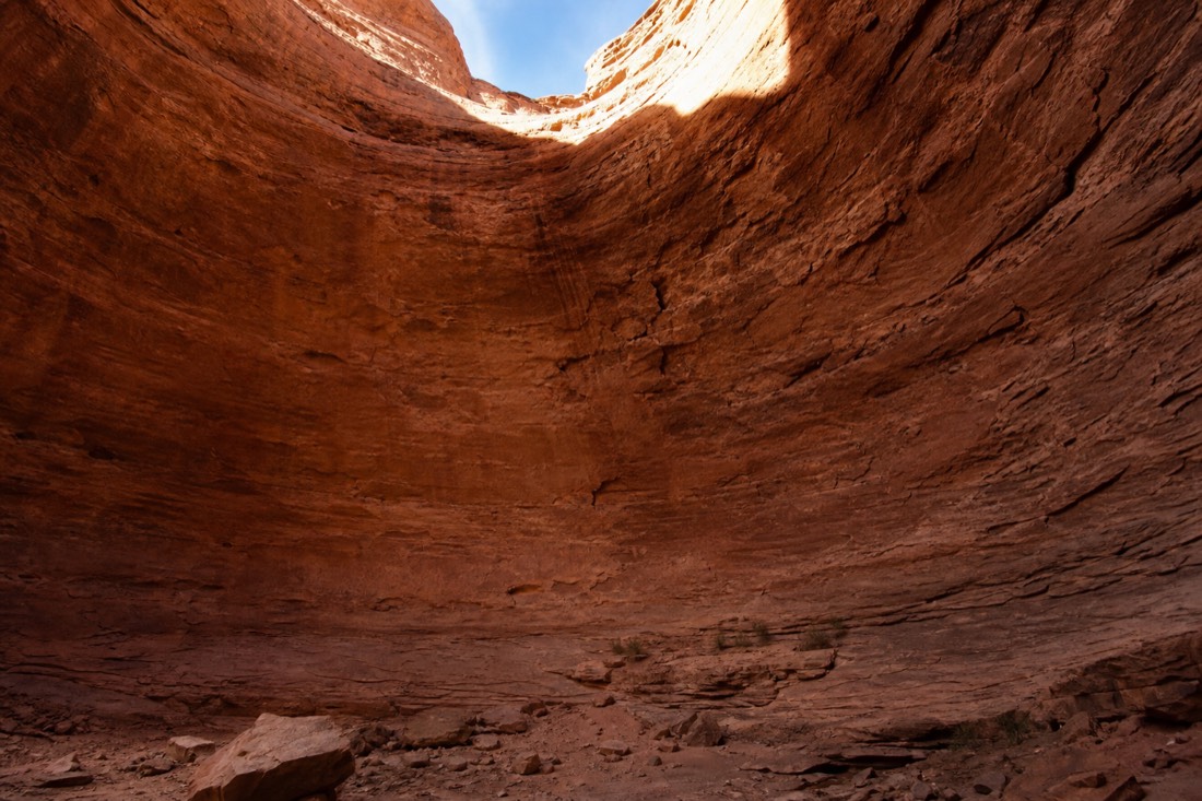 Inside the Big Hogan sandstone chamber, curved amphitheater walls opening upward to a shaft of daylight