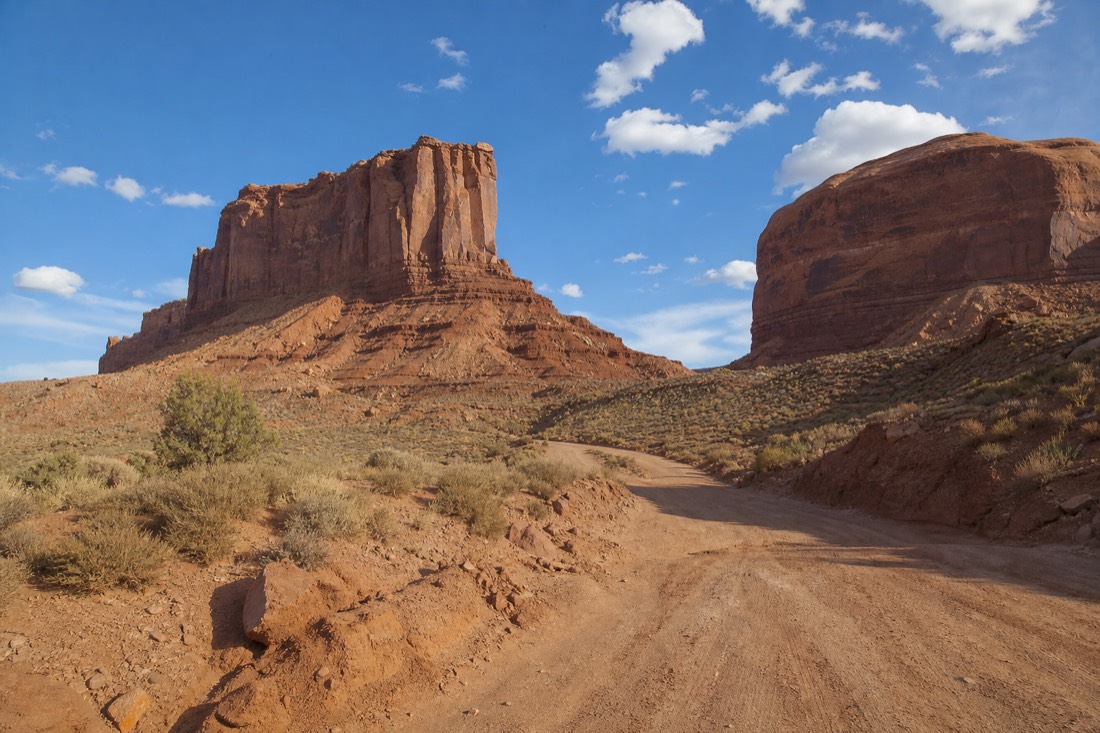 A rough dirt washboard road curving between towering red buttes on the 17-mile Valley Drive under a bright midday sky