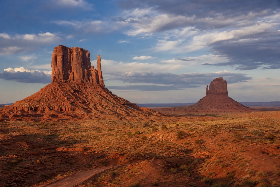The West and East Mitten buttes rising from the red valley floor beneath a wide dramatic desert sky