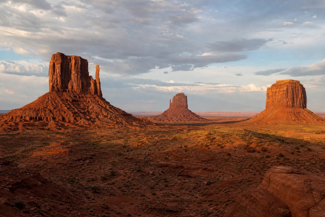 A cinematic wide Western vista of Monument Valley buttes rising across a vast open desert plain under a dramatic sky