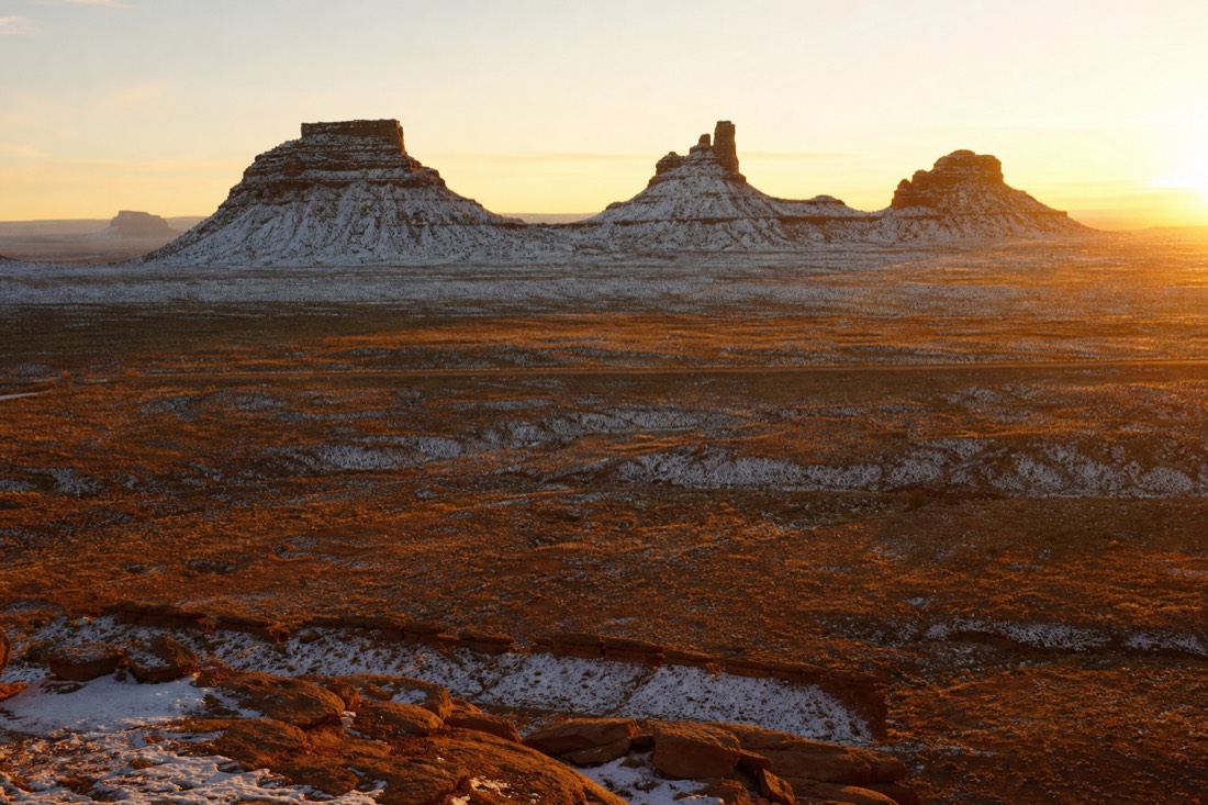 Low golden winter afternoon sun setting behind snow-flecked buttes casting very long shadows across the valley floor