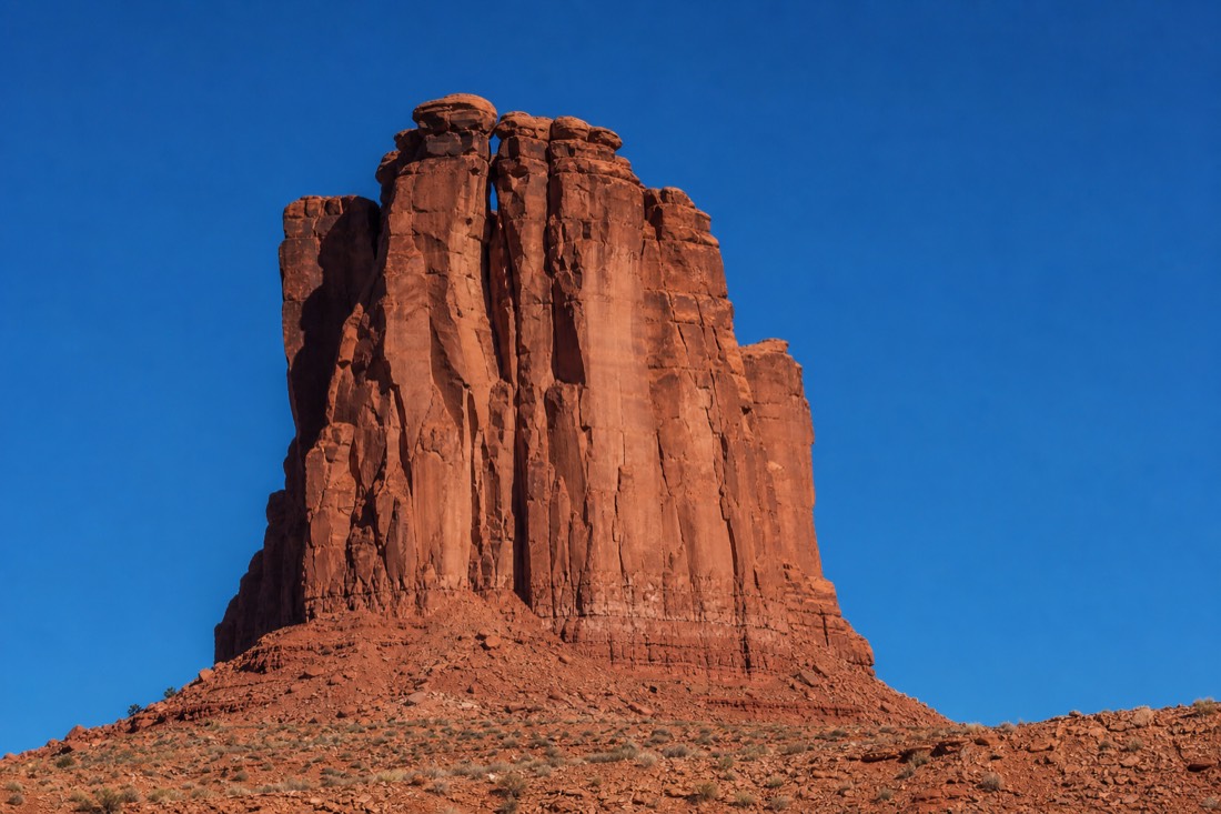A single isolated sandstone butte compressed against a polarized deep-blue desert sky in a telephoto frame