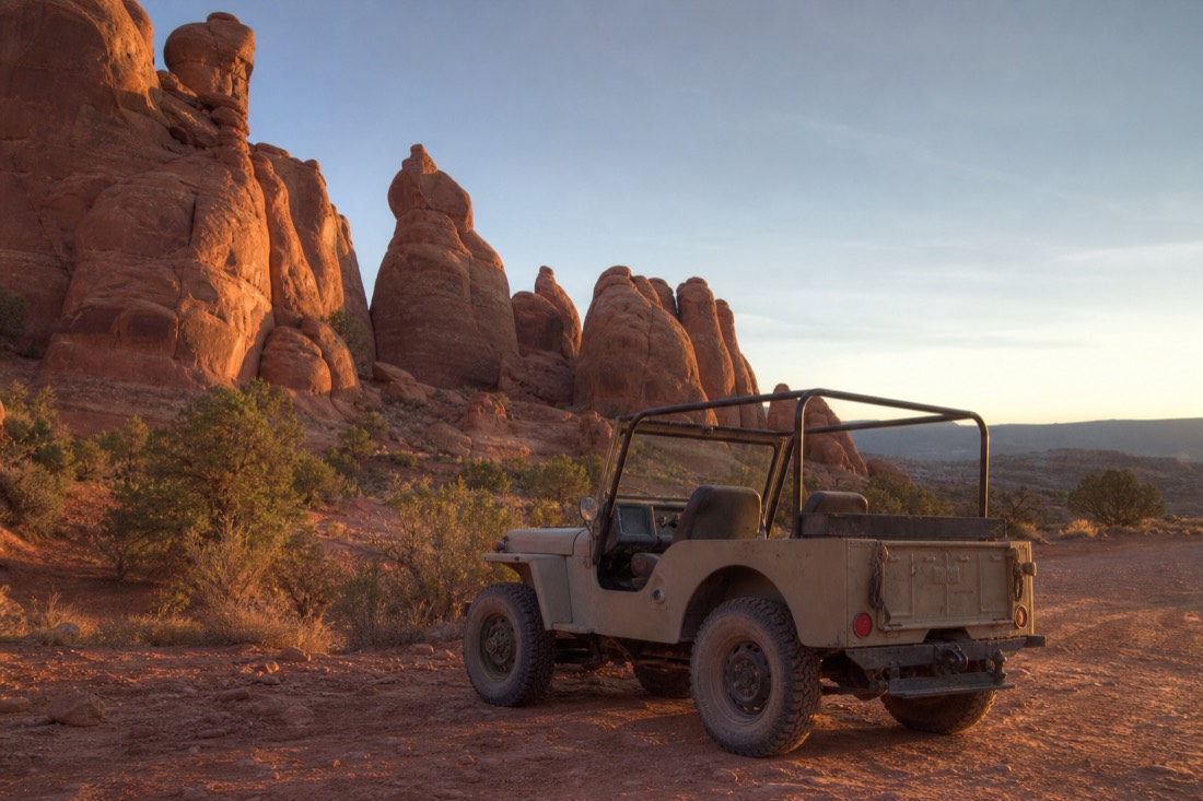 An open-air Navajo jeep parked among the backcountry sandstone spires in soft early-morning light