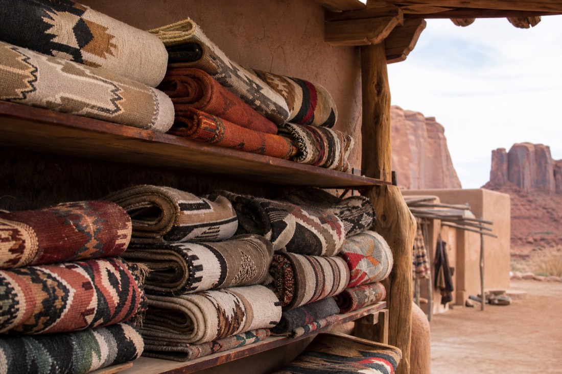 Rolled Navajo wool rugs displayed on shelves inside a rustic trading post with adobe walls