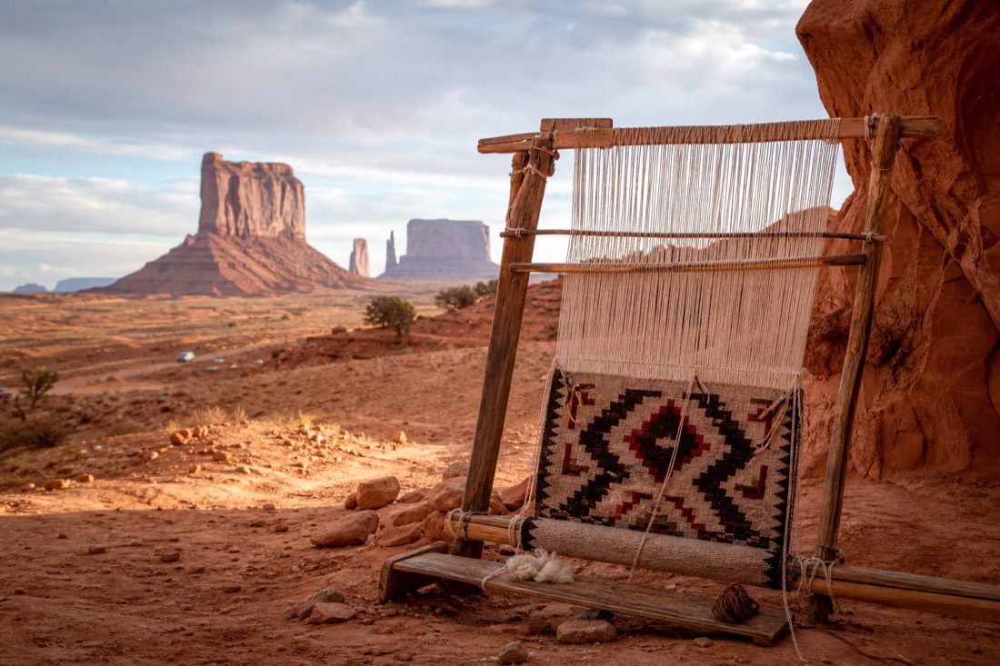 A traditional Navajo weaving loom with a partly finished rug set against the red rock of Monument Valley