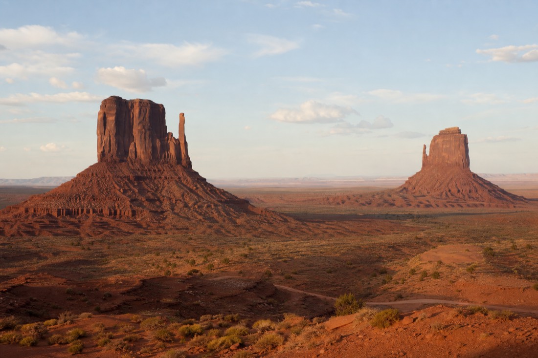The East and West Mitten Buttes standing alone on the flat red desert floor of Monument Valley