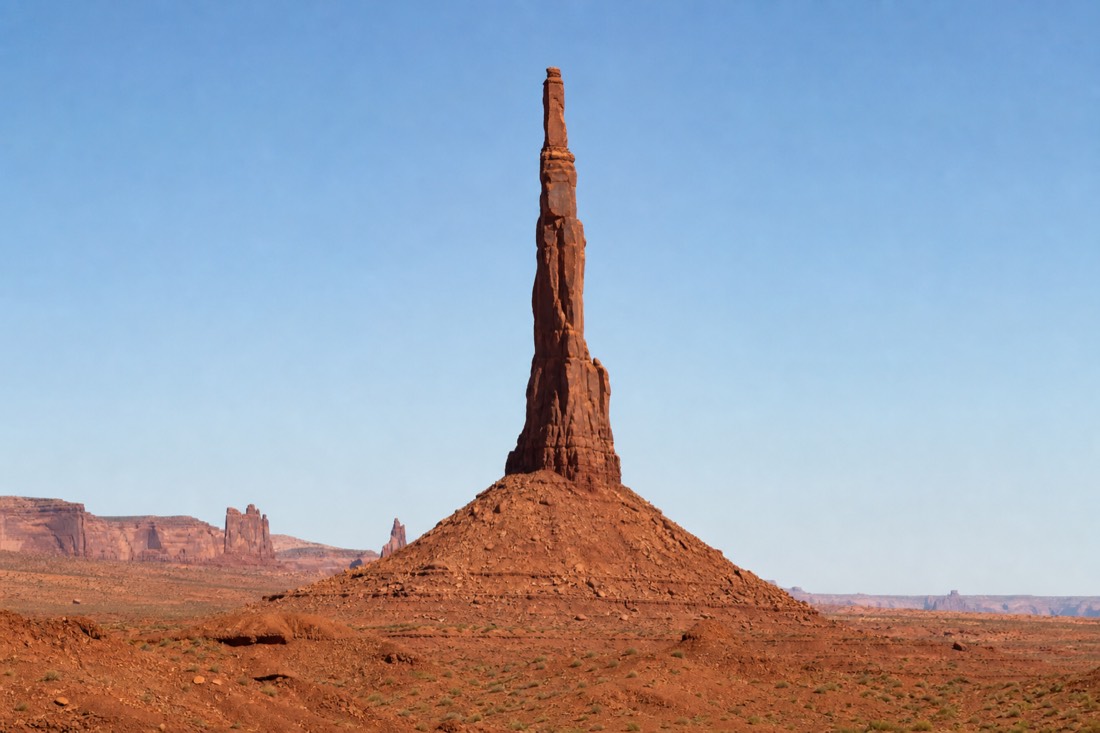 The slender Totem Pole spire rising needle-thin against a clear sky in Monument Valley