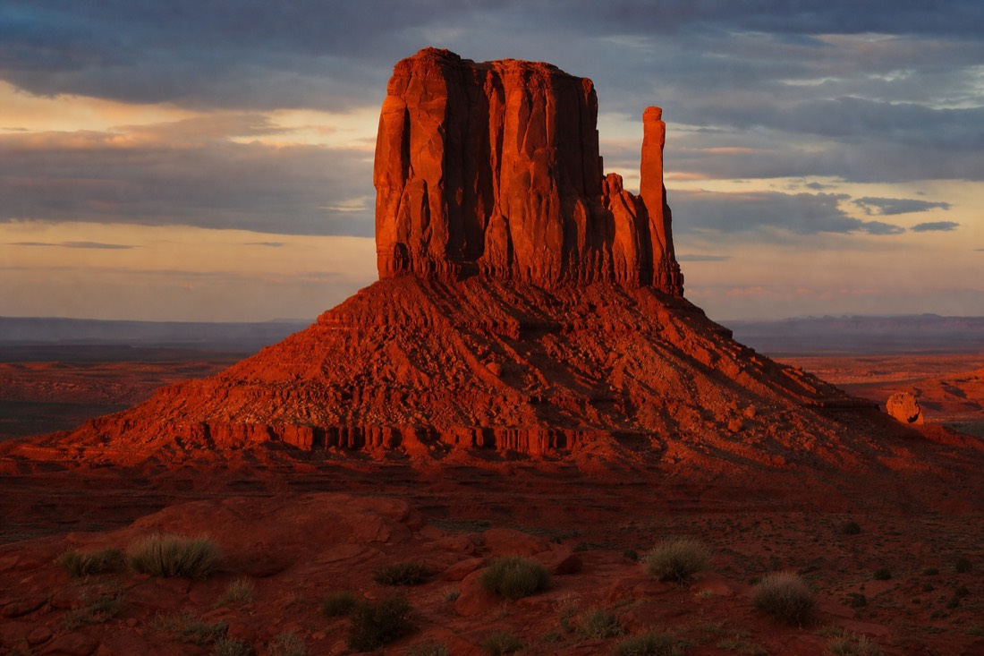 Low warm sunset light turning a Monument Valley butte deep orange-red against a darkening sky