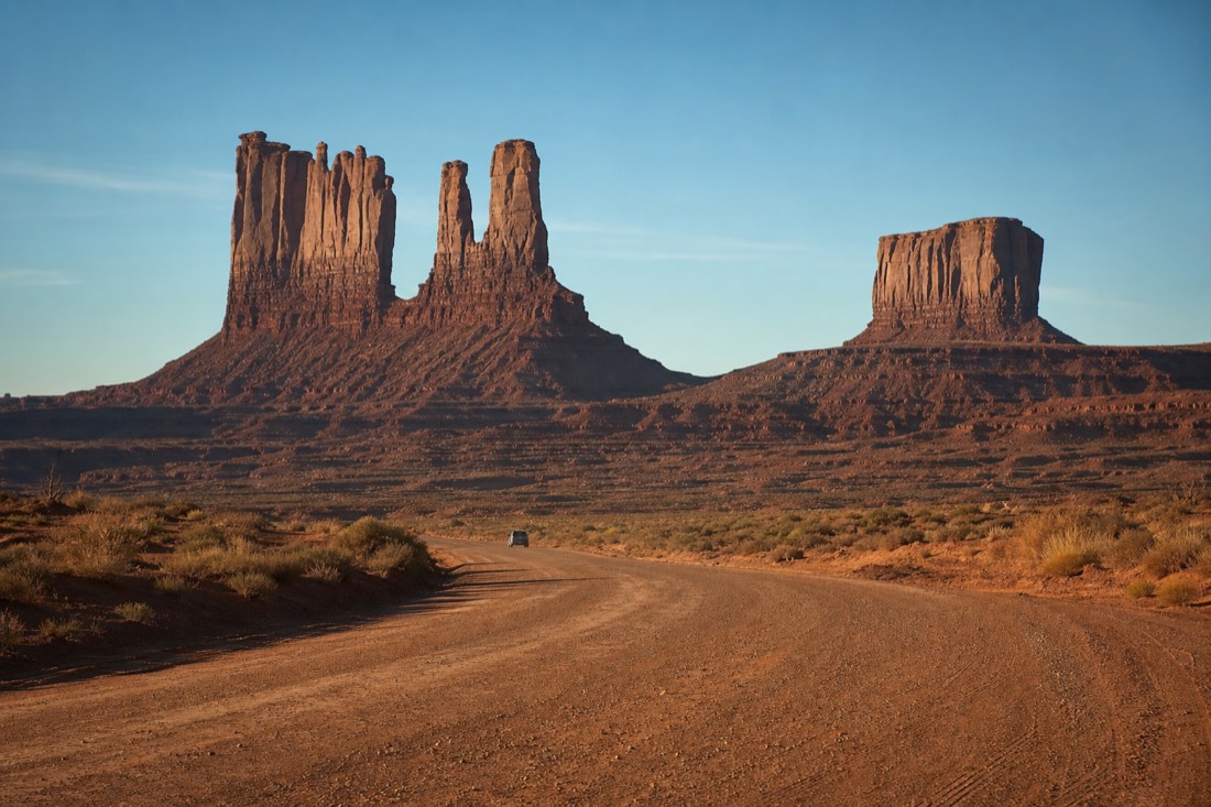 The Mittens and Merrick Butte rising above the red dirt 17-mile Valley Drive with a lone car on the road