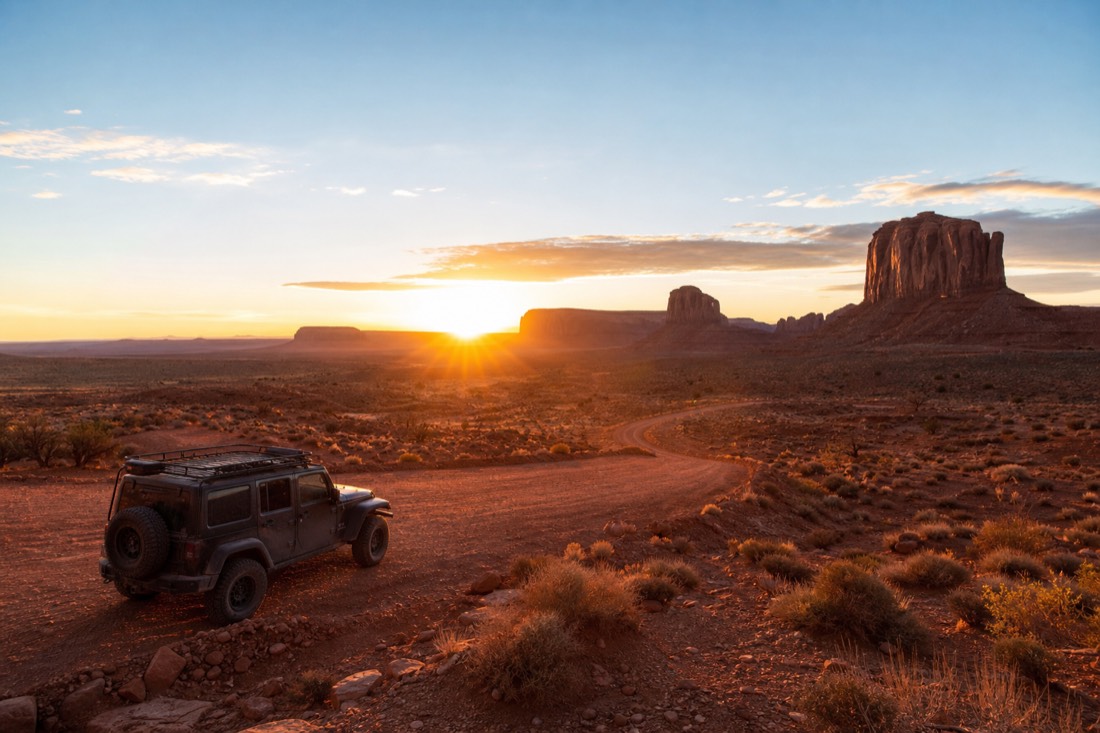 Sunrise breaking over the buttes with a Navajo jeep parked on the red dirt loop road