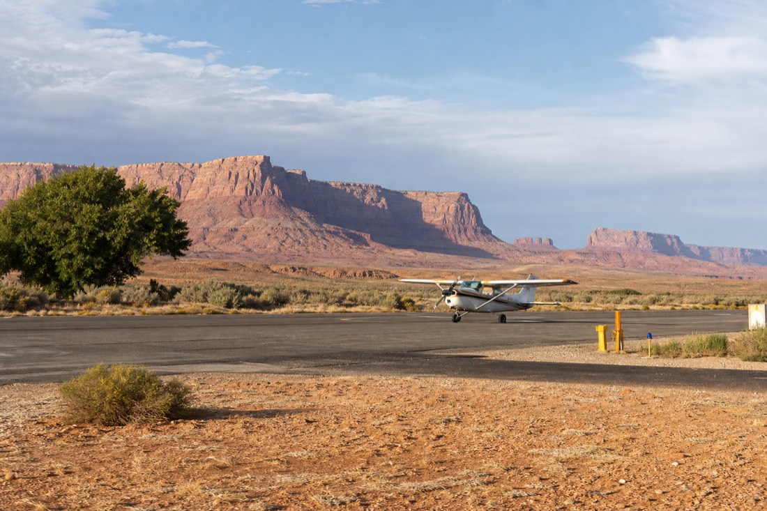 A small regional desert airstrip with a light aircraft on the tarmac and red rock plateaus far in the distance