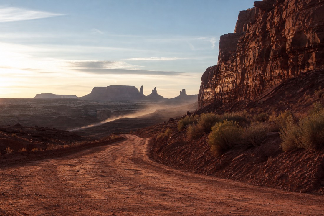 The unpaved washboard red dirt Valley Drive descending toward the Mitten buttes, a faint dust trail rising
