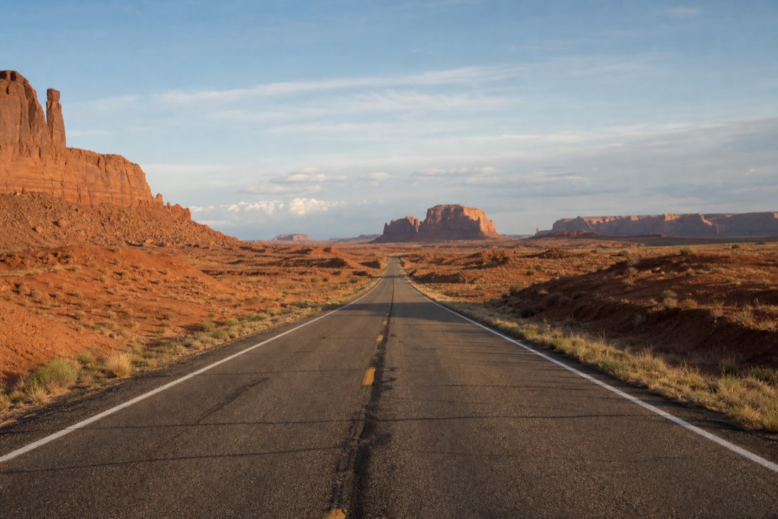 Empty two-lane desert highway crossing open red-rock country between parks