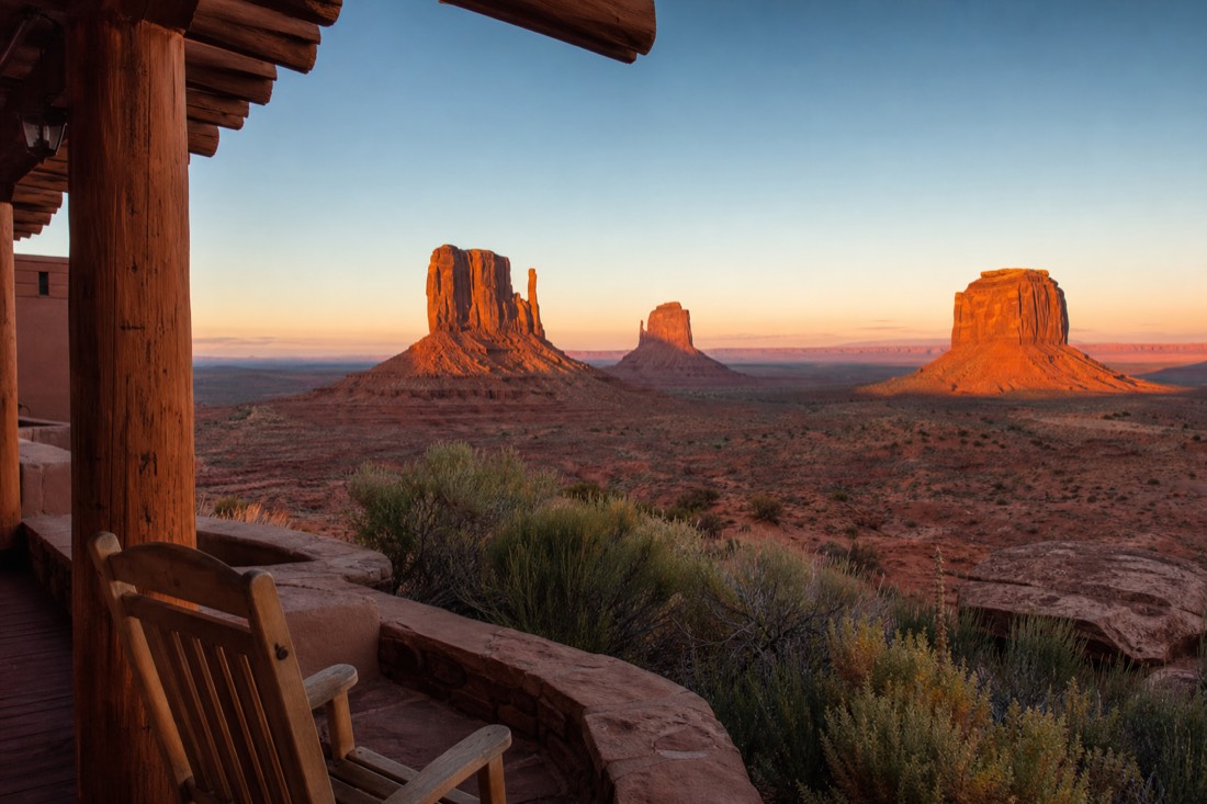 A lodge terrace at dawn overlooking the Mitten buttes as the first light turns the sandstone warm orange