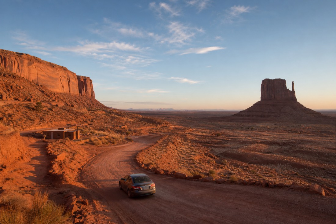 A lone car starting down the first red dirt descent toward the West Mitten Butte past the visitor center