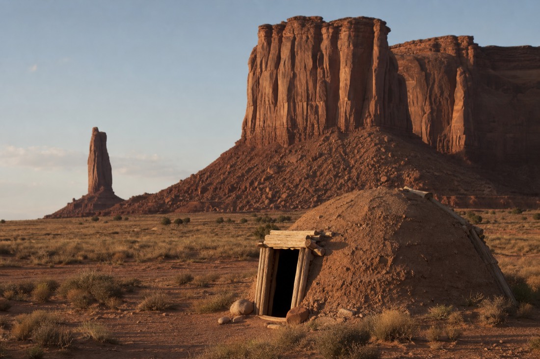 A traditional Navajo hogan on the valley floor with red sandstone buttes standing behind it