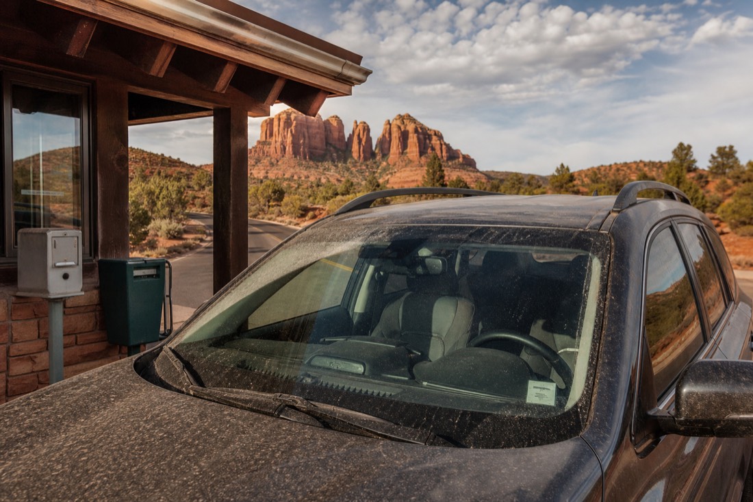 A dusty parked rental SUV at the Tribal Park entrance booth with red sandstone buttes framed through the windshield