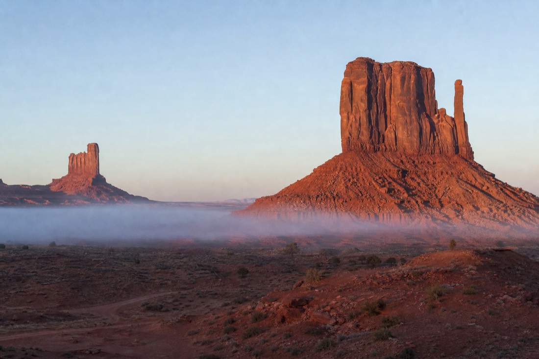 Red sandstone buttes under a wide plateau sky with morning haze cooling the desert floor