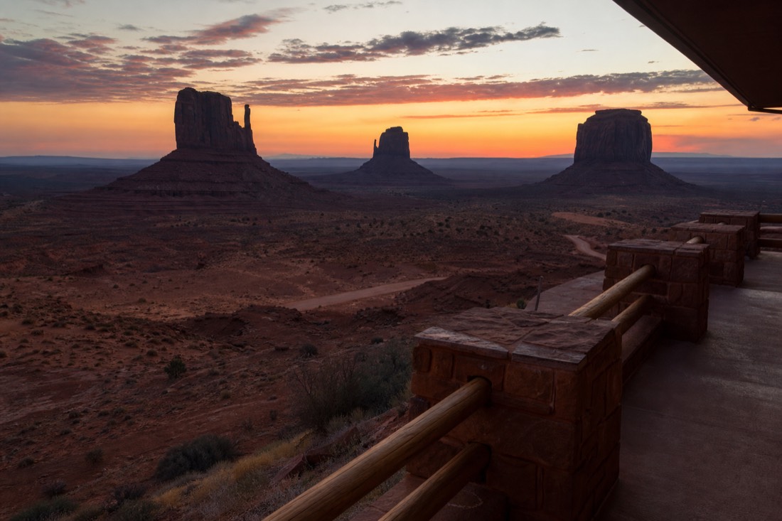 A lodge terrace at dusk overlooking the mitten buttes as the sky turns orange over the darkening valley