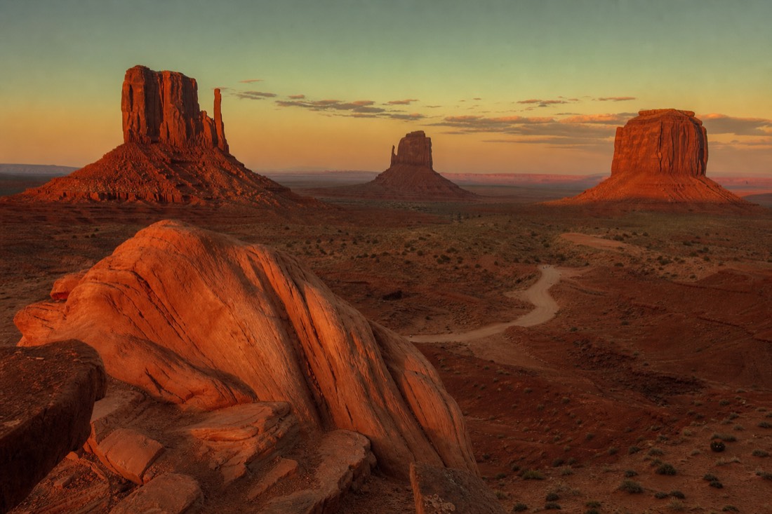 Cinematic wide Western vista of Monument Valley buttes at golden hour framed like a classic film