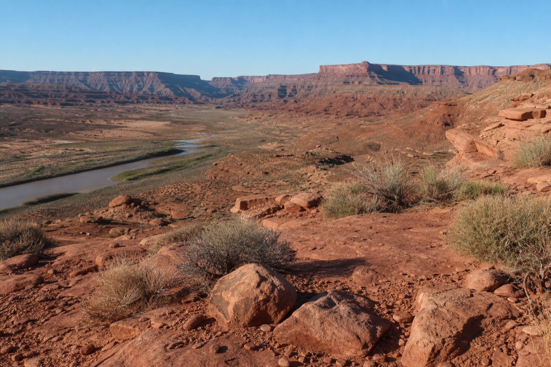 Sun-baked high-desert overlook with sparse brush and shadeless red rock terrain