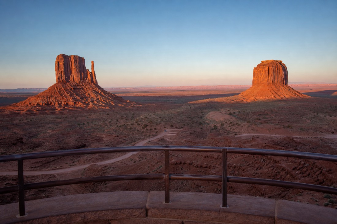 Empty balcony railing above the visitor center looking straight at the sunlit West and East Mitten buttes at dawn