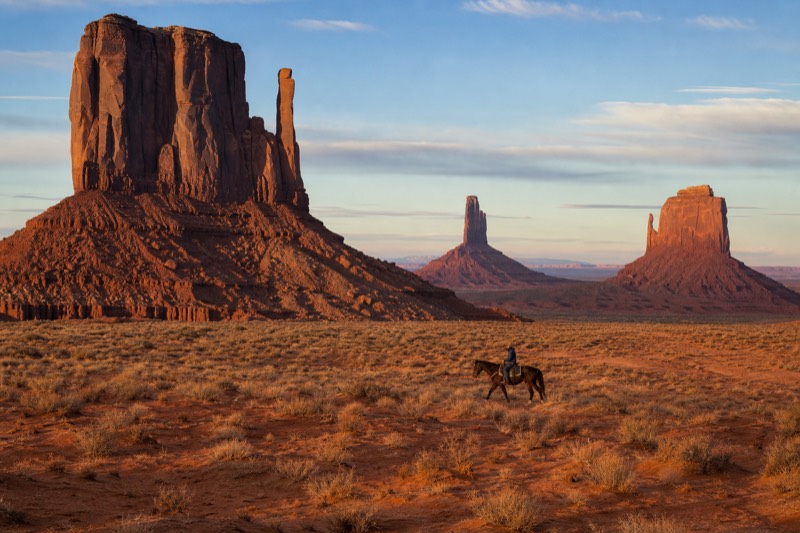 A rider on horseback with a Navajo guide crossing the red desert floor beneath Monument Valley's buttes