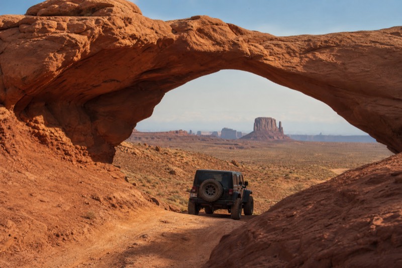A backcountry 4x4 jeep tour passing a sandstone arch in the restricted Navajo backcountry of Monument Valley