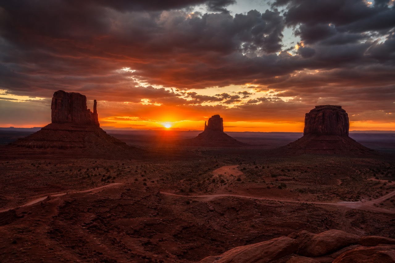 The buttes of Monument Valley glowing deep red under a dramatic sunset sky